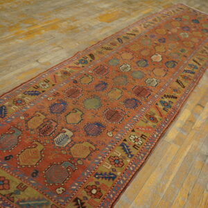Rust runner rug featuring repeating geometric medallions and a floral border on worn wooden floorboards.