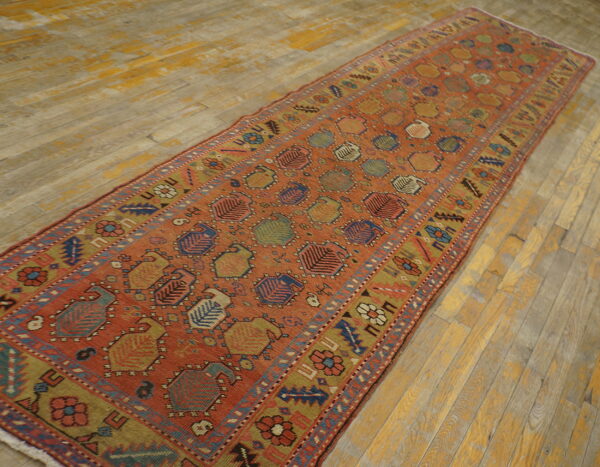 Rust runner rug featuring repeating geometric medallions and a floral border on worn wooden floorboards.
