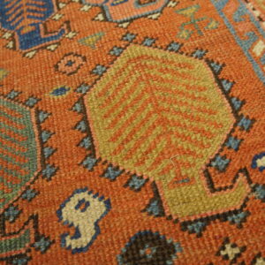 Rust orange rug detail showing geometric patterns in gold, teal, cobalt blue, and cream colors.