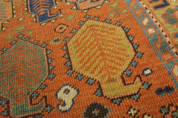 Rust orange rug detail showing geometric patterns in gold, teal, cobalt blue, and cream colors.