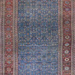 Intricate patterned rug with a blue central field and a wide, geometric rust red primary border.