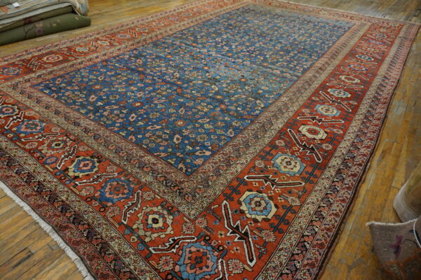 Blue floral patterned rug with wide orange-red borders displayed on natural hardwood flooring.