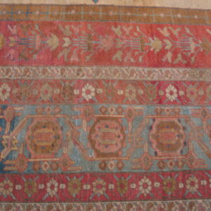 Intricate low-pile rug close-up featuring horizontal stripes of dusty red, faded blue, and tan patterns.