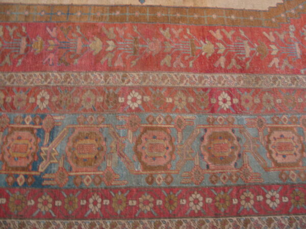 Intricate low-pile rug close-up featuring horizontal stripes of dusty red, faded blue, and tan patterns.