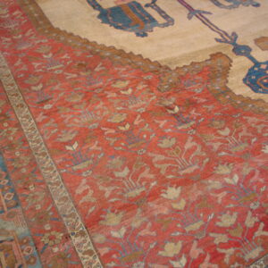 Close view of a rug's red floral field, blue patterned borders, and a large cream center with blue motifs.
