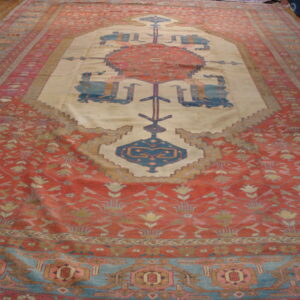 Faded red field rug featuring a cream stepped medallion with geometric blue and rust motifs on wood floors.