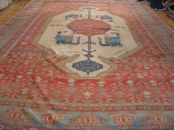 Faded red field rug featuring a cream stepped medallion with geometric blue and rust motifs on wood floors.
