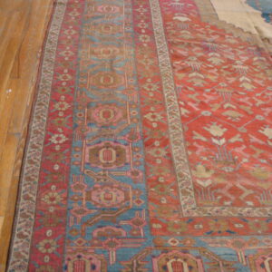 Rust red and blue geometric patterned rug with pink accents lying on a shiny wooden floor.