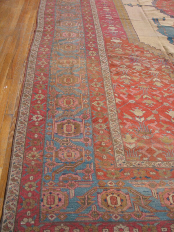 Rust red and blue geometric patterned rug with pink accents lying on a shiny wooden floor.