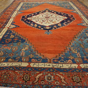 Orange and blue central medallion rug featuring stepped spandrels and inscribed cartouches on wood plank flooring.