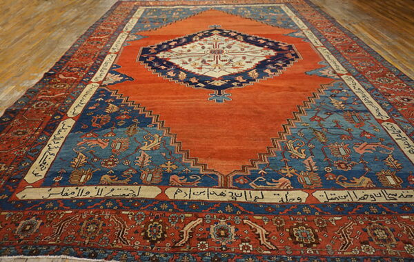 Orange and blue central medallion rug featuring stepped spandrels and inscribed cartouches on wood plank flooring.