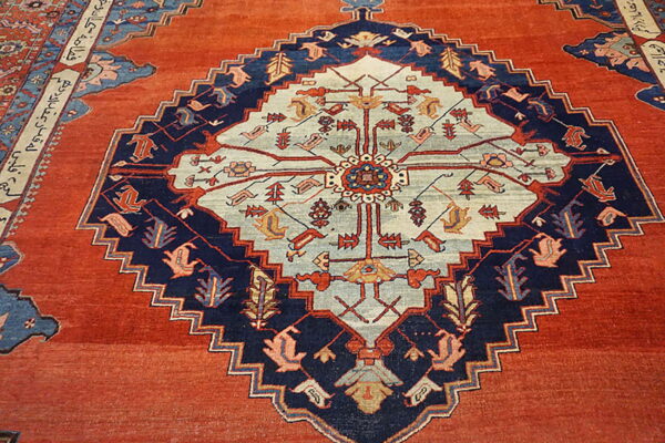 Rust rug with a large, stepped navy and pale blue geometric medallion and a detailed script border.