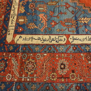 Red and blue patterned rug showing script cartouches and animal motifs rests on light wood plank flooring.
