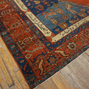 Intricate red and blue rug with script borders lies diagonally on worn wooden floorboards.