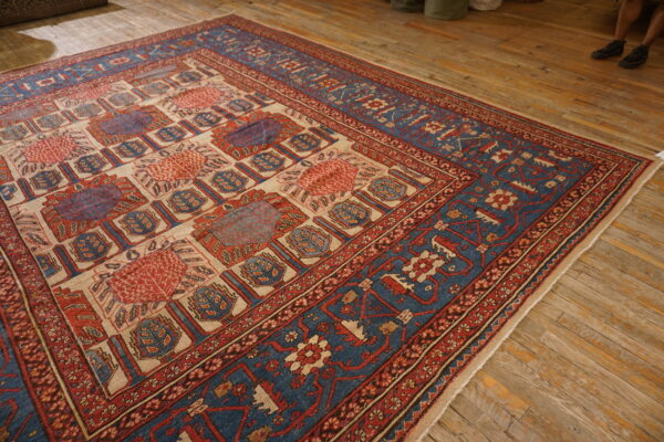 Geometric red, blue, and cream patterned rug laid out on a rustic, wide plank wood floor.