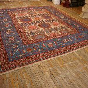 Blue, red, and cream traditional rug with geometric motifs displayed on distressed hardwood flooring in a warehouse setting.