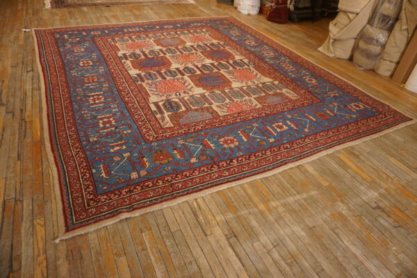 Blue, red, and cream traditional rug with geometric motifs displayed on distressed hardwood flooring in a warehouse setting.