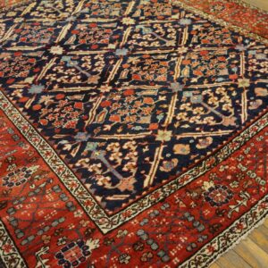 Intricate floral rug featuring a dark blue field and a wide terracotta red border on wood planks.