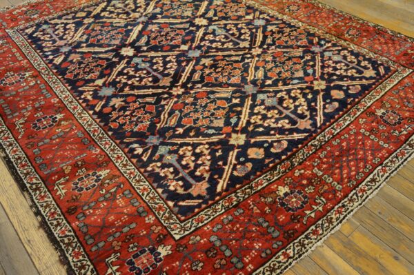 Intricate floral rug featuring a dark blue field and a wide terracotta red border on wood planks.