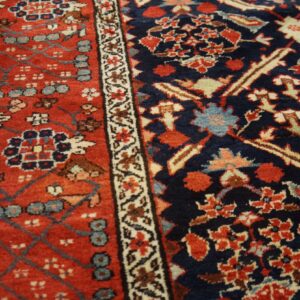 High-pile rug detail showing complex navy and brick red floral patterns resting on dark wood flooring.
