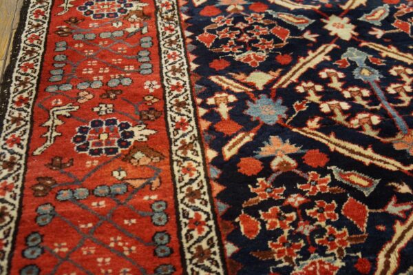 High-pile rug detail showing complex navy and brick red floral patterns resting on dark wood flooring.