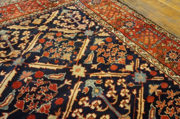 Detailed view of a navy and red floral rug with high pile on light wooden floorboards.