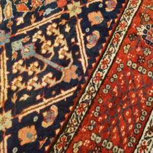 Detailed close-up of a high-pile rug with navy blue, red, and beige ornate patterns on wood floors.