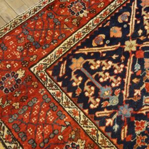 Low pile rug detail featuring dense red, navy, and cream floral patterns over light wood flooring.