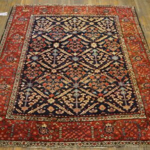 Traditional navy blue and red ornate rug with a dense geometric pattern sits centered on rustic hardwood flooring.