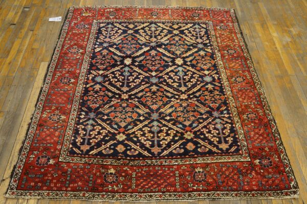 Traditional navy blue and red ornate rug with a dense geometric pattern sits centered on rustic hardwood flooring.