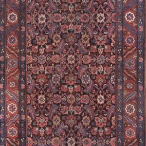 Intricate, dark-ground runner rug with dense floral motifs and wide red and navy blue borders.