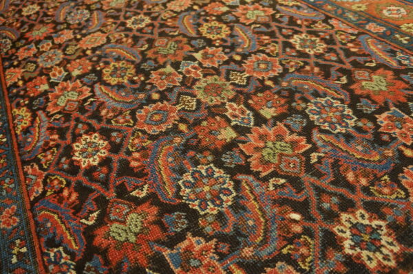 Traditional low-pile rug with dense red, blue, and green floral motifs on a dark field.