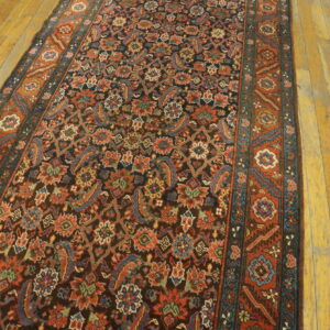 A dark runner rug with dense floral patterns in red, blue, and green lies on a worn wooden floor.