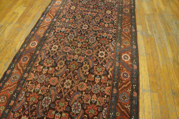 A dark runner rug with dense floral patterns in red, blue, and green lies on a worn wooden floor.