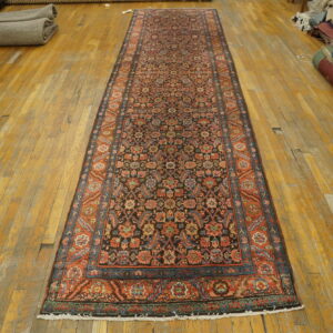 Long runner rug with a black, rust, and blue traditional pattern laid on a distressed wooden floor.