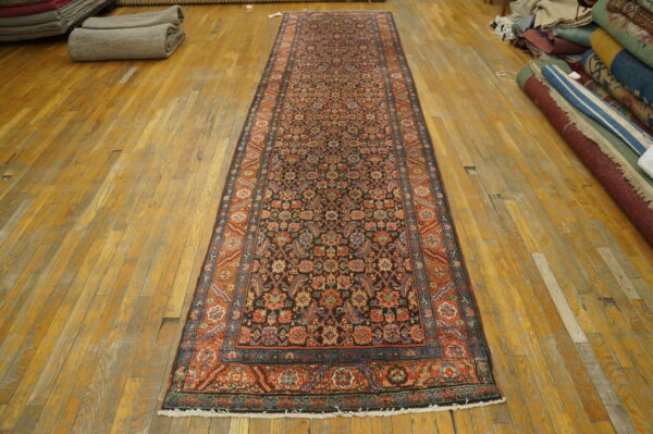 Long runner rug with a black, rust, and blue traditional pattern laid on a distressed wooden floor.