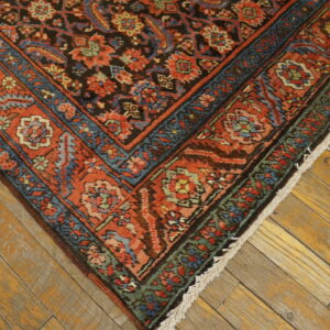 Ornate rug with rust, blue, and black floral patterns resting on rustic wood plank flooring.