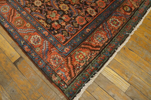 Ornate rug with rust, blue, and black floral patterns resting on rustic wood plank flooring.
