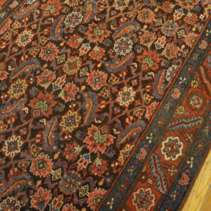 Intricate floral rug featuring a dark field and rust red, teal, and blue accents resting on distressed wood floors.