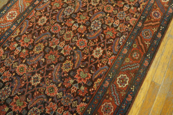 Intricate floral rug featuring a dark field and rust red, teal, and blue accents resting on distressed wood floors.