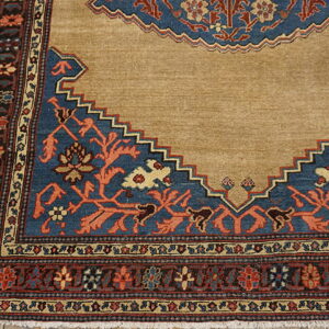 Tan rug corner featuring a stepped blue medallion design with rust floral motifs and multi-banded borders.