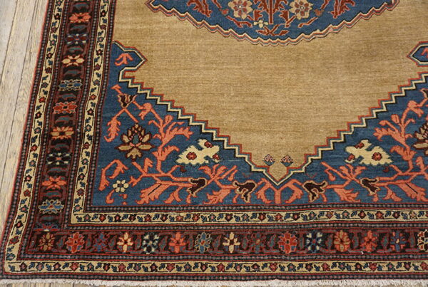 Tan rug corner featuring a stepped blue medallion design with rust floral motifs and multi-banded borders.