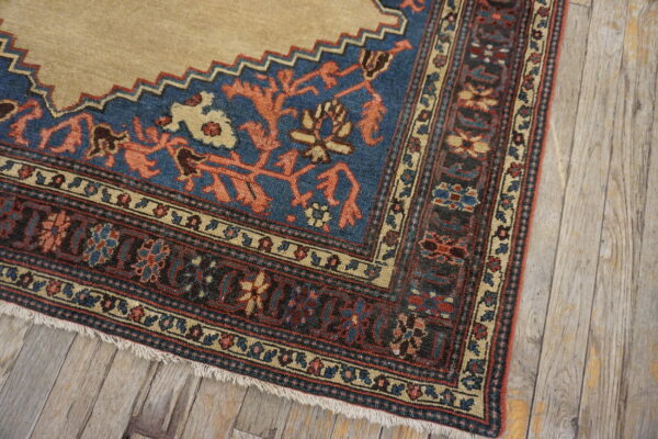 Low-pile rug detail showing tan field, blue panel, and patterned borders on rustic wood flooring.