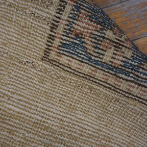 The textured tan rug backing is visible, rolled to show a blue and rust geometric pattern on wood floors.