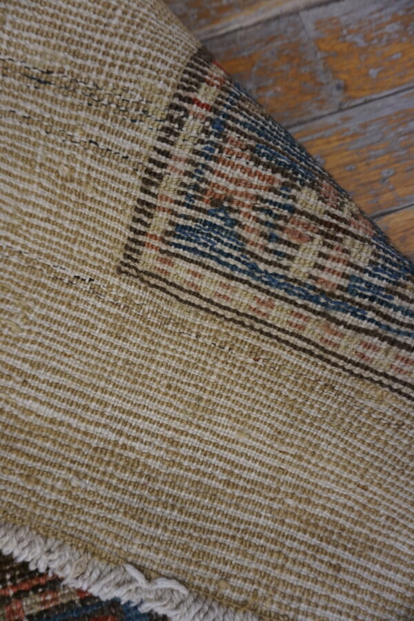 The textured tan rug backing is visible, rolled to show a blue and rust geometric pattern on wood floors.