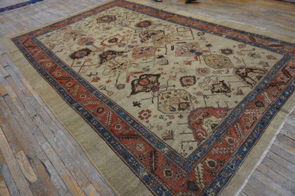 Beige rug featuring geometric motifs, bordered by intricate rust red and navy blue patterns on wood floors.
