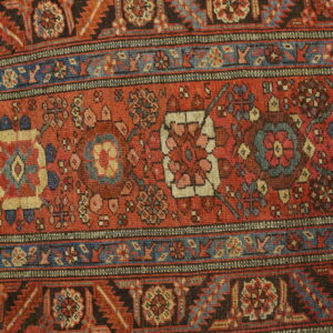 Red and dark blue rug with repeating geometric and floral medallions resting on light wood floors.