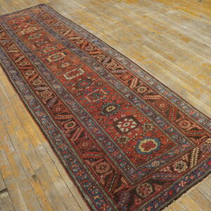 Red and blue patterned runner rug with geometric designs laid on worn, light wood planks.