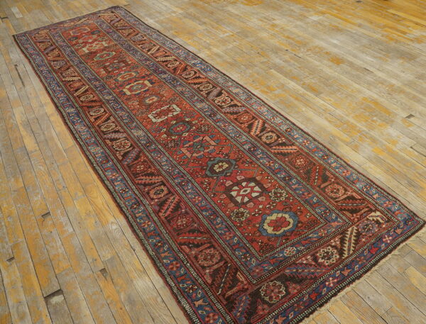 Red and blue patterned runner rug with geometric designs laid on worn, light wood planks.