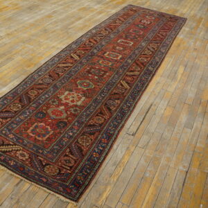 Red and blue patterned runner rug with geometric designs is displayed on light, distressed wood plank flooring.